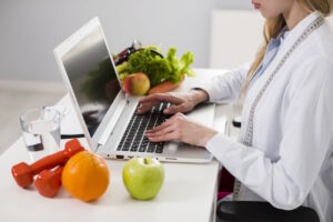 Imagem mostra mulher com computador e frutas à mesa, para simular como abrir CNPJ para nutricionista